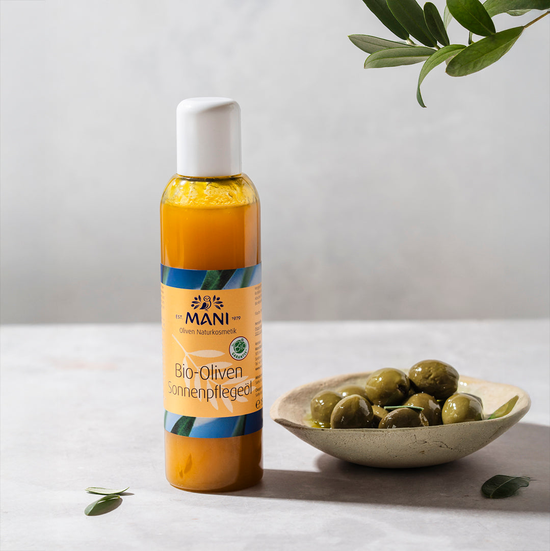 MANI Bio Oliven Sonnenpflegeöl neben Schälchen mit Oliven