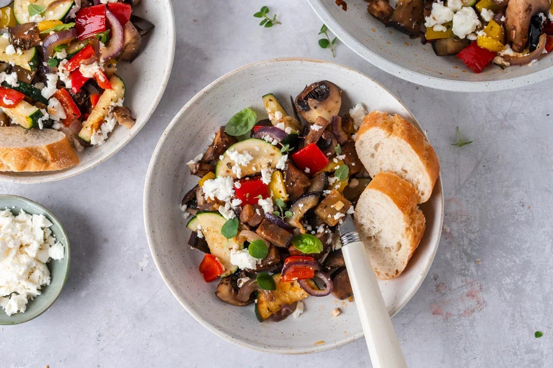 mediterrane Gemüsepfanne mit Feta und Weißbrot auf Tellern