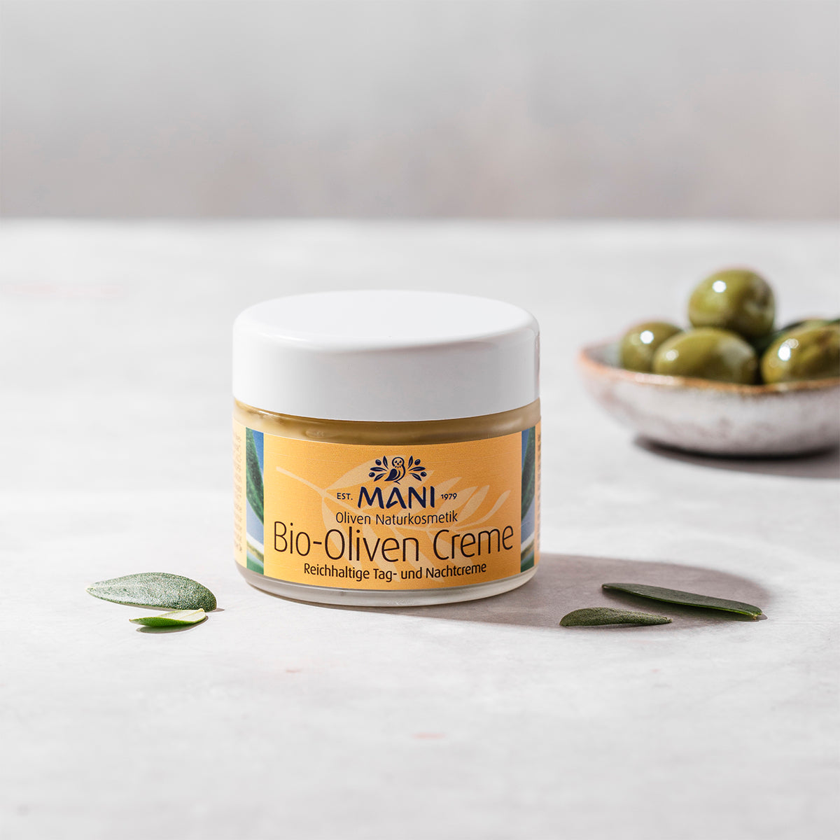 MANI Bio Olivencreme und Schälchen Oliven im Hintergrund