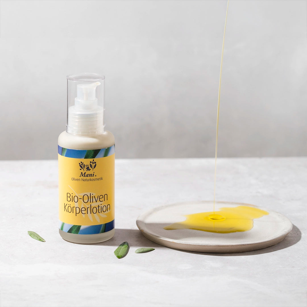 MANI Bio Oliven Körperlotion neben Teller mit Olivenöl und Olivenblättern