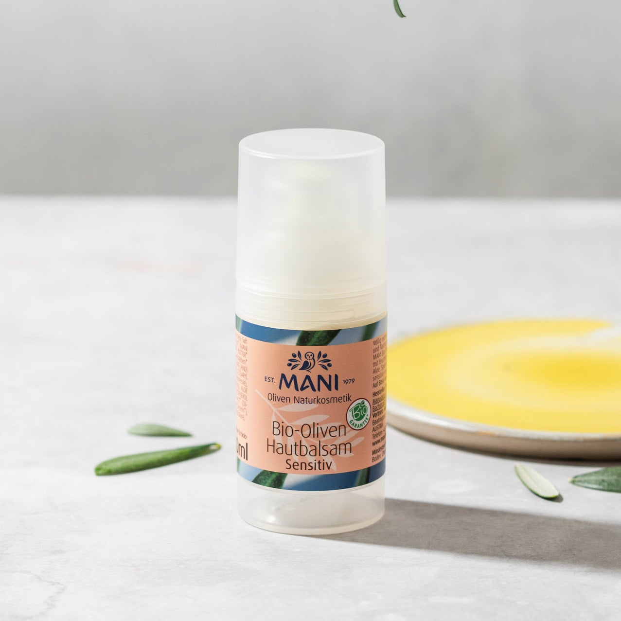 MANI Bio Oliven Hautbalsam neben Teller mit Olivenöl und Olivenblätter