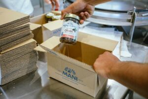 MANI Mitarbeiter verpackt ein Glas MANI Oliven in einen Karton für den Versand.